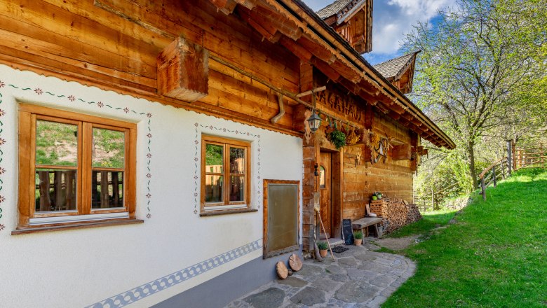 Traditionelles Haus mit viel Holz, dekorativen Fenstern und Deko neben einer gr&uuml;nen Wiese.
