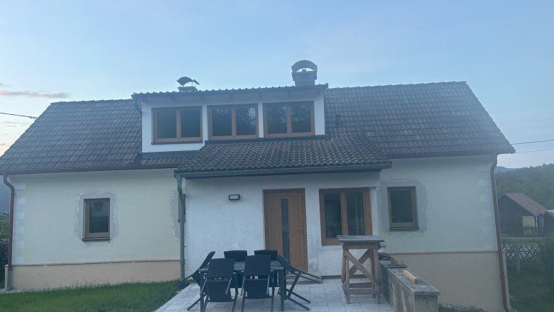 Ein zweist&ouml;ckiges Ferienhaus mit Dachschindeln und Terrasse, umgeben von Rasen und l&auml;ndlicher Umgebung.