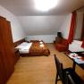 Ein einfach eingerichtetes Zimmer mit Doppelbett, Sofa, Tisch und Stuhl. Holzmöbel und orangefarbene Vorhänge dominieren den Raum.