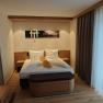Modern eingerichtetes Doppelzimmer mit einem gro&szlig;en Bett, Holzm&ouml;beln und einem gro&szlig;en Fenster mit Vorh&auml;ngen.
