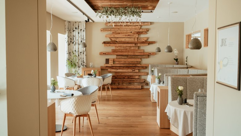 Innenansicht eines eleganten Restaurants mit Holzboden, modernen Möbeln und dekorativen Holzelementen an der Wand.