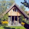 Ein gemütliches Holzferienhaus mit Terrasse, umgeben von Bäumen und Blumen.