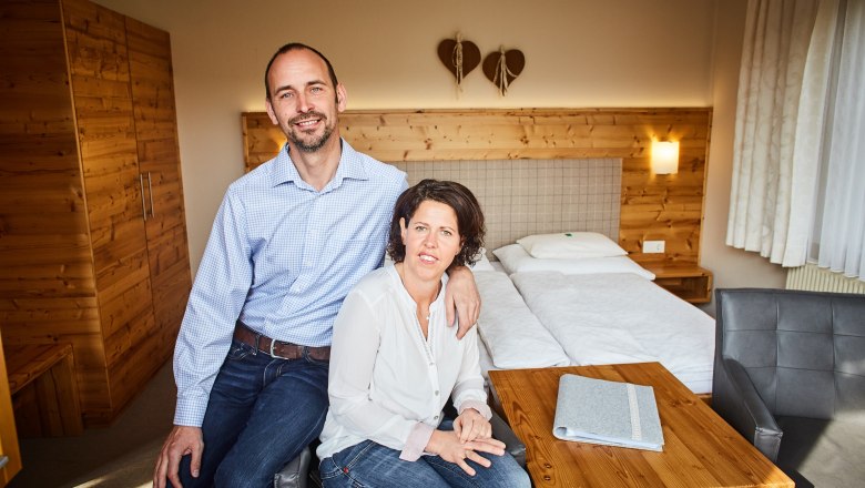Ein Paar sitzt in einem gemütlichen Zimmer mit Holzmöbeln und einem Doppelbett.
