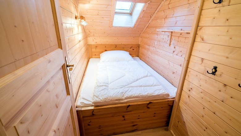 Kleines Kinderzimmer mit Holzverkleidung, Einzelbett und Dachfenster.