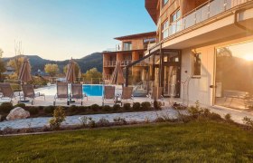 Au&szlig;enbereich des Naturhotel Molzbachhof mit Pool und Liegest&uuml;hlen bei Sonnenuntergang.