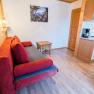 Wohnzimmer mit rotem Sofa, Holzwänden und kleiner Küche.