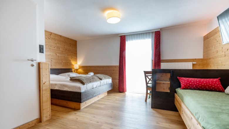 Gemütliches Hotelzimmer mit Holzwänden, Doppelbett, Einzelbett und rotem Vorhang.