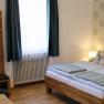 Gemütliches Doppelzimmer mit Bett, Kleiderschrank, Tisch, Stuhl und Fenster mit blauen Vorhängen.