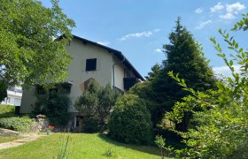 Ein zweist&ouml;ckiges Haus mit Garten und B&auml;umen, bei sonnigem Wetter.