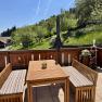 Terrasse mit Holzm&ouml;beln und Blick auf gr&uuml;ne Wiesen und B&auml;ume.