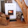 Innenraum eines Ferienhauses mit Kamin, Holzstapel, Korbsessel und Holztreppe.