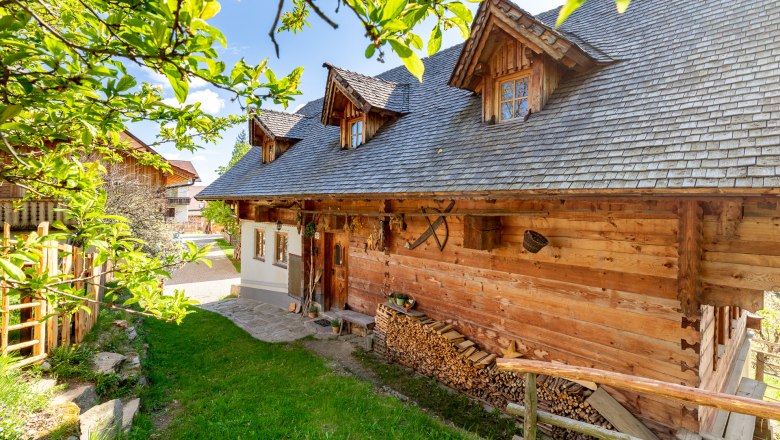 Traditionelles Holzhaus mit Holzstapel und Holzzaun umgeben von gr&uuml;ner Natur.
