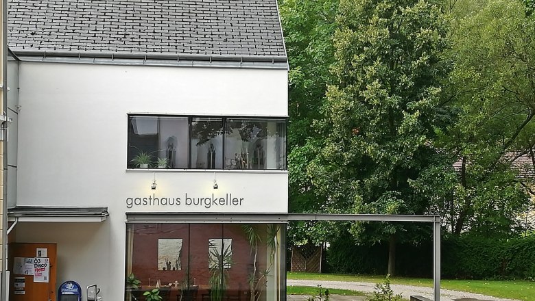 Modernes Gebäude mit der Aufschrift 'Gasthaus Burgkeller', umgeben von Bäumen.
