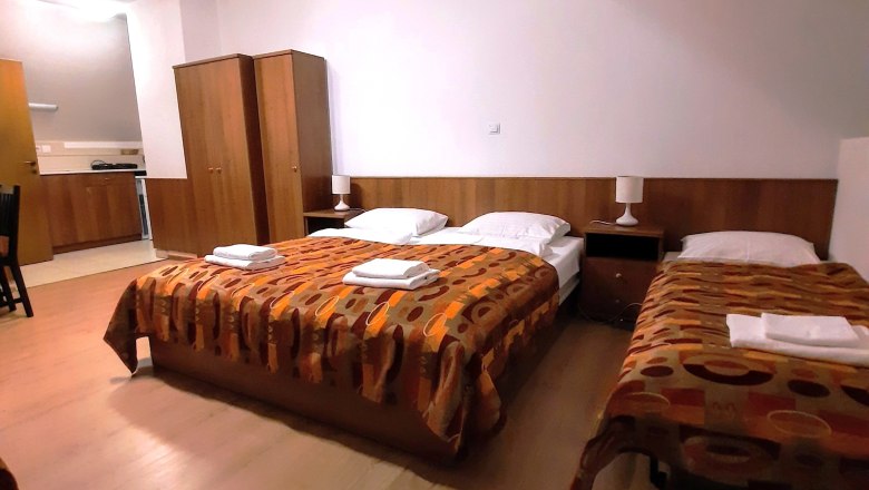 Ein Dreibettzimmer mit zwei Einzelbetten und einem Doppelbett, alle mit gemusterten Decken. Ein Kleiderschrank und Nachttische sind ebenfalls vorhanden.