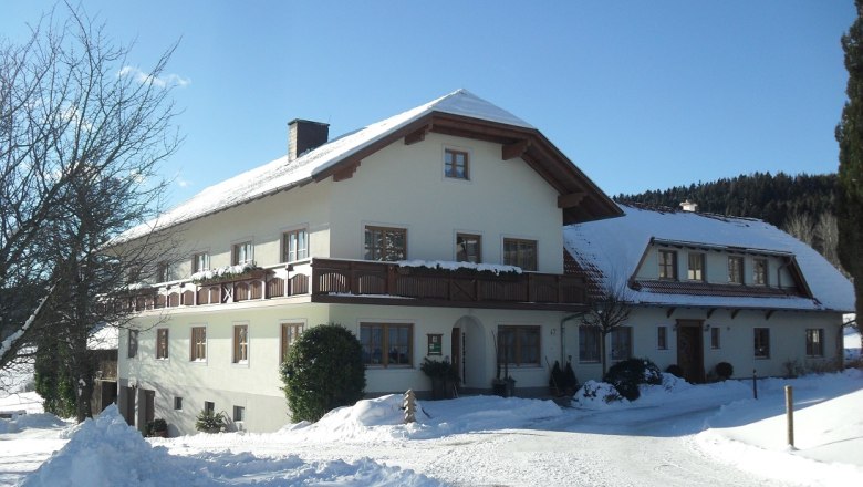 Ein großes Bauernhaus im Winter mit Schnee bedeckt, unter blauem Himmel.