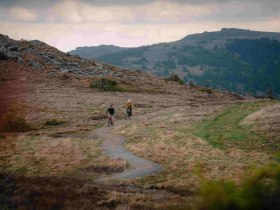 Zwei Mountainbiker fahren auf einem schmalen Pfad in einer bergigen Landschaft.