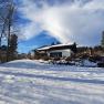 Winterlandschaft mit einem Haus im Schnee, umgeben von Bäumen und blauem Himmel.
