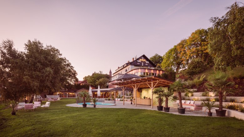 Ein gro&szlig;es Geb&auml;ude mit Terrasse und Garten bei Sonnenuntergang.