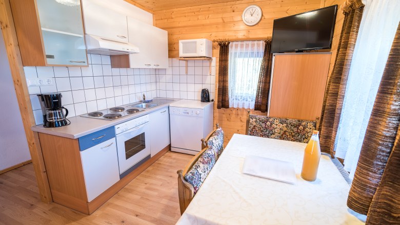 Gemütliche Küche mit Holzwänden, Esstisch, Herd, Kaffeemaschine und Fernseher.