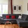 Modernes Wohnzimmer mit grauem Sofa, roten Kissen, Glastisch und Kunstwerken an der Wand.