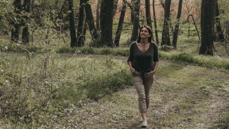 Frau spaziert auf einem Waldweg, umgeben von Bäumen und Grün.