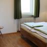Schlafzimmer mit Doppelbett, Fenster mit grünen Vorhängen, Sofa, Tisch, Tapete und einer Wandlampe.
