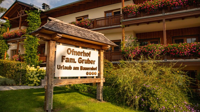 Schild vor einem Bauernhof mit Blumen und Holzveranda.