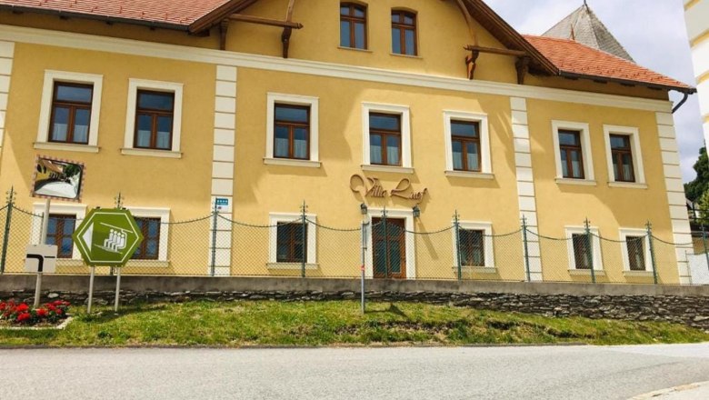 Gelbes Geb&auml;ude mit der Aufschrift 'Villa Luef', umgeben von einem Zaun und einer Stra&szlig;e im Vordergrund.