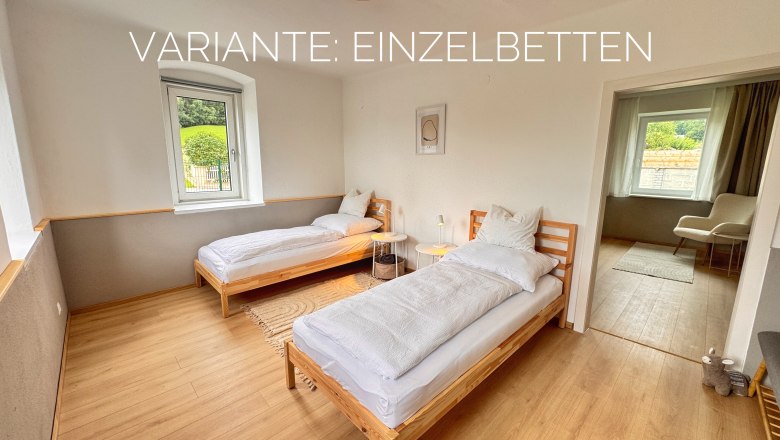 Schlafzimmer mit zwei Einzelbetten, Holzboden und Fenster mit Blick nach drau&szlig;en.