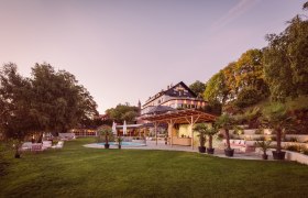 Gro&szlig;es Haus mit Garten und Pool bei Sonnenuntergang.