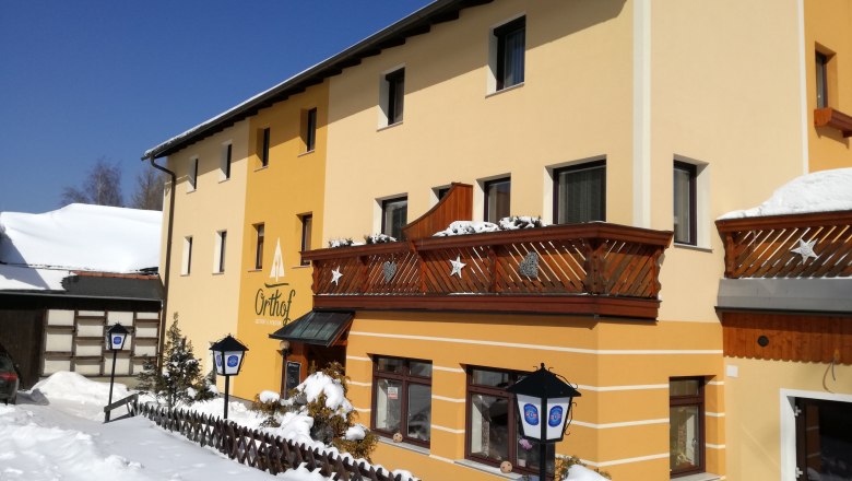 Gelbes Gebäude mit Holzbalkonen im Schnee, blauer Himmel.