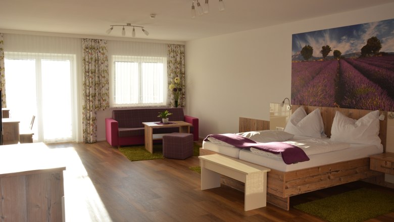 Ein modernes Doppelzimmer mit Holzboden, einem großen Bett, einer Sitzecke und einem Bild von Lavendelfeldern an der Wand.