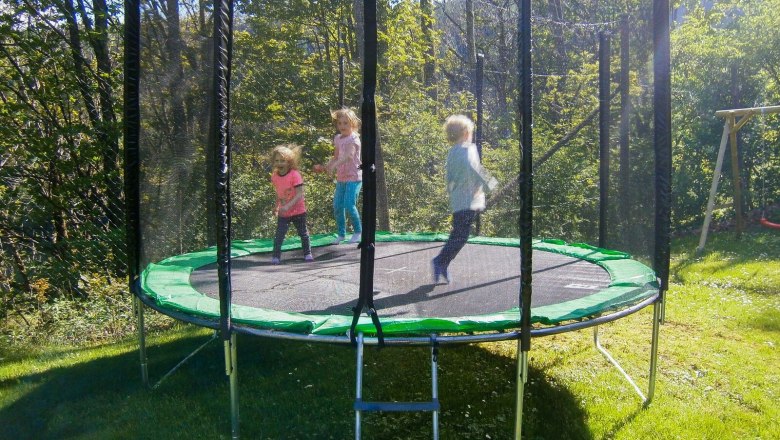 Drei Kinder springen auf einem Trampolin im Freien.