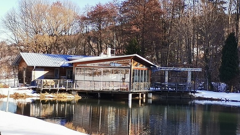 Ein Restaurant am Ufer eines Teiches im Winter, umgeben von B&auml;umen.