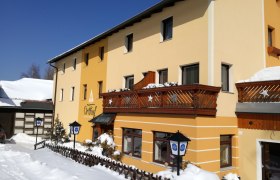 Gelbes Gebäude mit Holzbalkonen im Schnee, blauer Himmel.