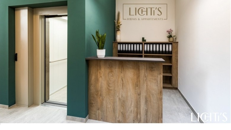 Empfangsbereich mit Holztheke, gr&uuml;nem Wandbereich und Aufzug.