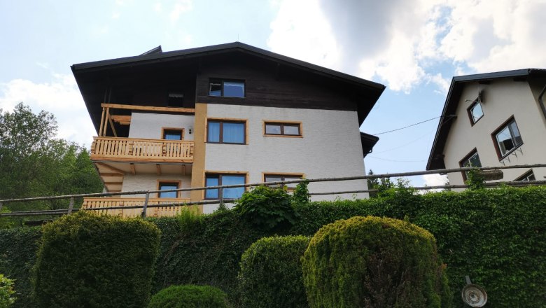 Zweist&ouml;ckiges Haus mit Holzbalkon und Garten im Vordergrund.