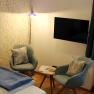Zimmer mit Bett, Tisch mit zwei Stühlen, Fernseher, Fenster mit blauen Vorhängen und Stehlampe.