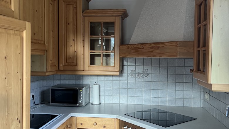 K&uuml;che mit Holzm&ouml;beln, Herd, Sp&uuml;le und Mikrowelle.